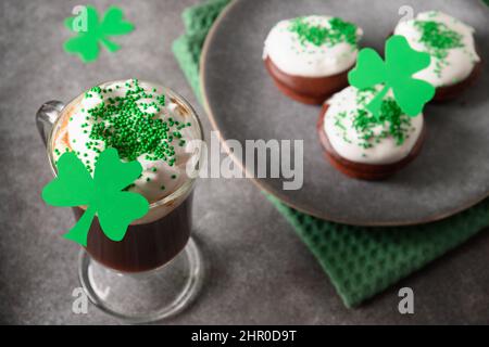 Irischer Kaffee in einer Tasse aus Glas und spezielle Cupcakes für den St. Patricks Day auf einem grauen Tisch. Alles gute zum St. Patrick Day. Stockfoto