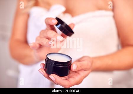 Nahaufnahme Einer Frau, Die Im Badezimmer Zu Hause Einen Feuchtigkeitsspender Aus Glas Anlegt Und Ein Handtuch Trägt Stockfoto