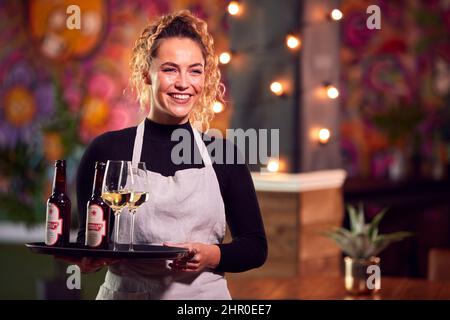 Porträt Eines Lächelnden Weiblichen Servers, Der Ein Tablett Mit Getränken In Der Cool Bar Oder Im Club Hält Stockfoto