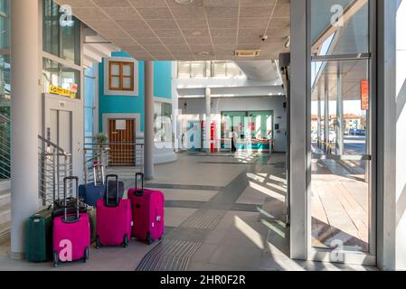 Fossano, Italien - 22. Februar 2022: Bahnhofskasse mit bunten Trolley-Koffern im Vordergrund Stockfoto