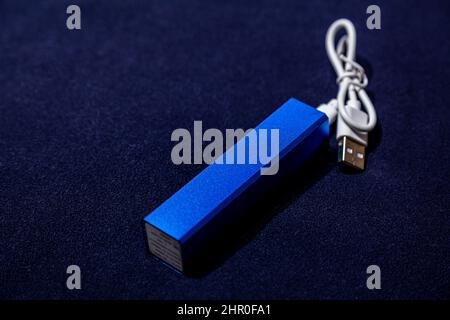 Blaues tragbares Ladegerät mit angeschlossenem usb-Kabel auf dunkelblauem Hintergrund Stockfoto