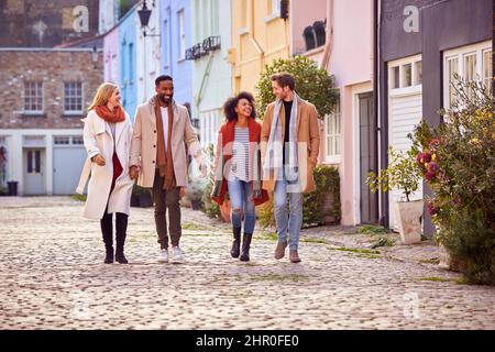 Multikulturelles Paar Mit Freunden, Das Im Herbst Oder Winter Entlang Der City Street Spazieren Geht Stockfoto