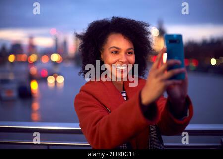 Frau Gegen Stadtlichter Im Freien Trägt Wintermantel Posiert Für Selfie Am Telefon Bei Dämmerung Stockfoto