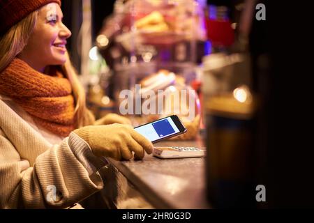 Frau, Die Kontaktlose Zahlungen Auf Dem Mobiltelefon Auf Dem Markt Im Freien Abgibt Stockfoto