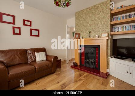 Cavendish, Suffolk - Jan 19 2019: Wohnzimmer im traditionellen Stil mit gemusterter Tapete an einer Wand, Ledersofa und Kamin. Stockfoto