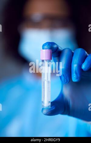 Laborarbeiterin in PSA mit Schutzbrille und Gesichtsmaske, die den Lateral Flow DNA-PCR-Test hält Stockfoto