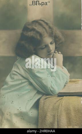 Ein süßes Mädchen sitzt am Tisch und lehnt sich an ihre Hände und denkt an etwas. Stockfoto