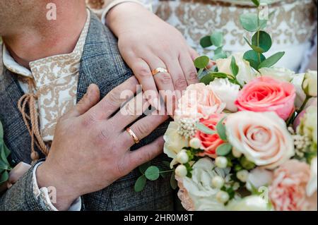 Goldene Eheringe, Hände der Braut und des Bräutigams auf einem Blumenstrauß Stockfoto