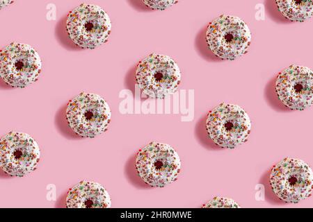 Köstliche glasierte Donuts auf dem rosa Tischhintergrund. Wiederholtes Muster, Draufsicht, Nahaufnahme. Stockfoto