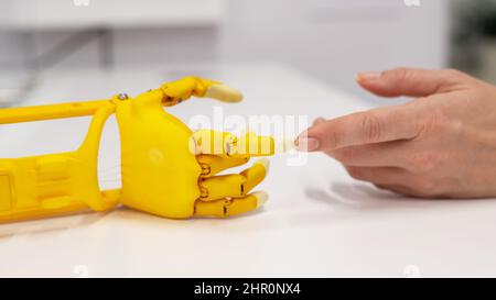 Frauenhand und eine Kunststoff-Handprothese für ein Kind auf weißem Hintergrund. Stockfoto