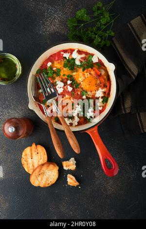 Shakshuka. Hausgemachte Spiegeleier mit Gemüse in eiserner Pfanne auf altem dunklen Schiefer, Stein oder Beton Hintergrund. Traditionelle Küche Israels. Spät Stockfoto