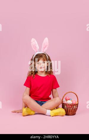 Mädchen in Osterhasen Ohren sitzen auf dem Boden in der Nähe Korb mit Ostereiern Stockfoto