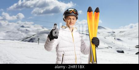 Junger Mann mit einem Paar Skiern und Daumen nach oben auf einen Berg gestikulieren Stockfoto