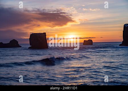 Blick auf Felsen und stürmisches Meer bei Sonnenuntergang von der Halbinsel Dyrholaey im Südosten Islands Stockfoto