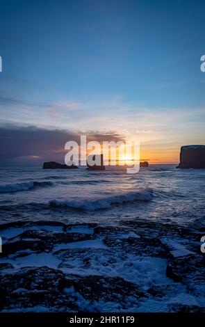 Blick auf Felsen und stürmisches Meer bei Sonnenuntergang von der Halbinsel Dyrholaey im Südosten Islands Stockfoto