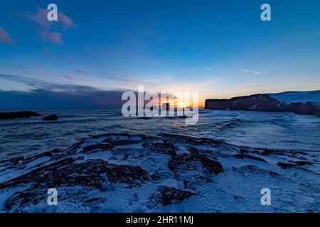 Blick auf Felsen und stürmisches Meer bei Sonnenuntergang von der Halbinsel Dyrholaey im Südosten Islands Stockfoto