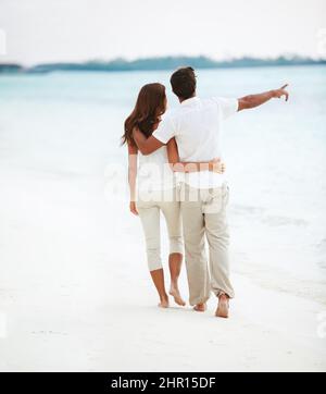 Ein romantischer, schöner Spaziergang. Rückansicht eines liebevollen jungen Paares, das auf das Meer zeigt, während Sie einen romantischen Spaziergang machen. Stockfoto