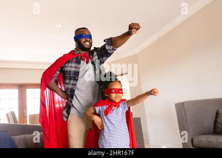 Lächelnder afroamerikanischer Vater und Tochter in Superhelden-Kostümen, die im Wohnzimmer spielen Stockfoto