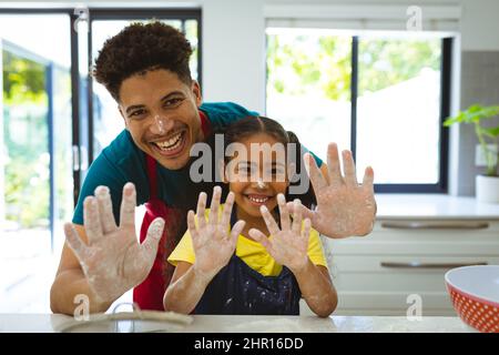 Porträt eines multirassischen Vaters und einer Tochter, die zu Hause mit Mehl bedeckte, schmutzige Hände zeigen Stockfoto