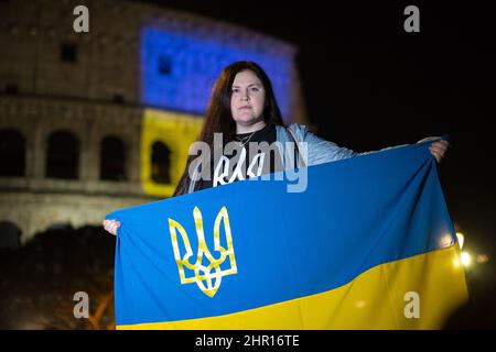 Rom Roma, Italien Italia. 24.. Februar 2022. Rom, 24.. Februar 2022. Die ukrainische Flagge wurde auf die Wände des Kolosseums in Rom projiziert, wo sich Menschen aus der ukrainischen Gemeinschaft versammelten, um ihre Fahnen zu schwingen, um gegen den Krieg gegen die Ukraine zu protestieren, der heute Morgen vom russischen Präsidenten Wladimir Putin erklärt wurde. Kredit: LSF Foto/Alamy Live Nachrichten Stockfoto