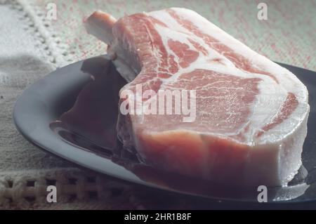 Rohe Schweinebone Steaks Tomahawk Schweinefleisch Steaks auf schwarzer Platte, Ansicht von oben. Drei rohe Schweinestäcke, bereit für Grill von oben. Stockfoto