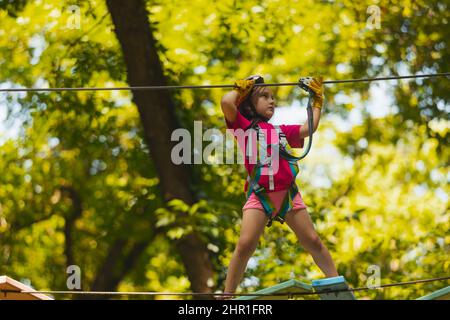 Das konzentrierte Mädchen überwindet sorgfältig Hindernisse im Seilpark Stockfoto