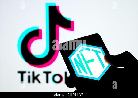 NFT-Logo auf dem Bildschirm des Smartphones und verschwommenes TikTok-Logo auf dem Hintergrund. Selektiver Fokus. Stafford, Großbritannien, 24. Februar 2022 Stockfoto