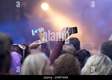 Den Moment festhalten. Rückansicht einer Menschenmenge bei einem Musikfestival, bei dem zwei Personen ihre Kameratelefone hochhielten. Stockfoto