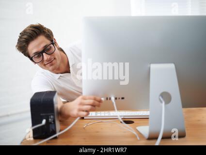 Ich habe das verstanden. Ein junger Mann, der ein Kabel an seinen Computer anschließt. Stockfoto