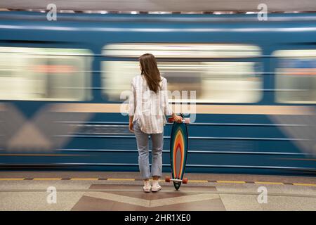 Mädchen warten auf U-Bahn-Auto am Bahnhof mit Zug auf Hintergrund. Rückansicht der Frau auf der Plattform Stockfoto