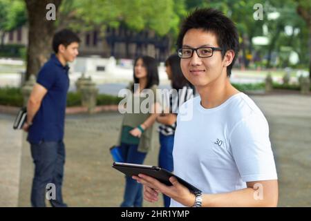 Mit moderner Technologie zum Studium für sein Finale. Porträt eines hübschen jungen Studenten, der draußen an seinem digitalen Tablet arbeitet. Stockfoto
