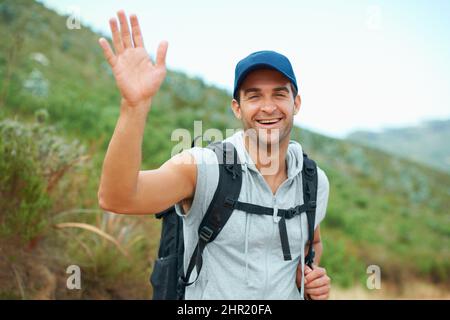 Auf Wiedersehen zum Stadtleben winken. Glücklicher junger Wanderer winkt der Kamera zu. Stockfoto