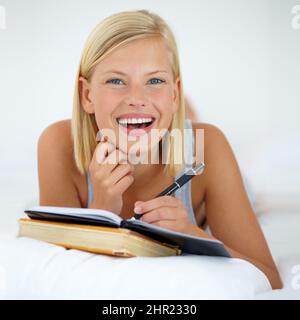 Ich weiß genau, was ich schreiben soll. Junge Frau, die zu Hause auf dem Bett lag und ihr Tagebuch schrieb. Stockfoto