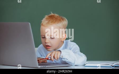 Schulkind mit digitalem pc-Laptop im Unterricht. Porträt von lustigen Schüler der Grundschule Studie Programmierung. Lustige blonde Pupille auf der Tafel. Stockfoto