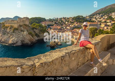 Mädchen ruht auf den oberen Wänden der Stadt Dubrovnik in Kroatien. Blick auf die Festung Fort Lovrijenac, über den Westhafen. Dubrovnik historische Stadt Kroatien in Stockfoto
