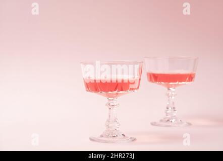 Zwei Kristallgläser Rosé-Sekt oder Champagner auf pastellrosa Hintergrund. Sommerdrink-Konzept. Minimale kreative Komposition mit Kopierplatz. Stockfoto