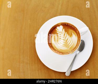 Von einem erfahrenen Barista zubereitet. Eine kunstvoll zubereitete Tasse Cappuccino auf einem Kaffeetisch. Stockfoto