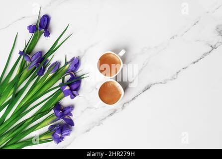 Zwei Tassen heißen Morgenkaffee in Form der Nummer 8 und ein Bouquet aus violetten Iris auf Marmorboden. Flach liegend mit Platz für Text. Grußkarte zum Frauentag und 8.. März. Stockfoto