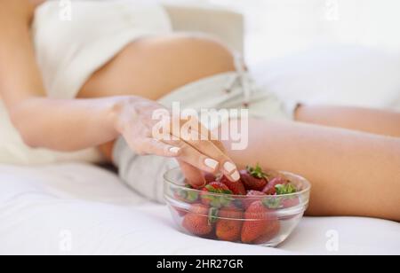 Immer die zusätzlichen Kalorien in Form von einem gesunden Snack. Zugeschnittenes Bild einer Schwangeren mit einer Schüssel Erdbeeren. Stockfoto