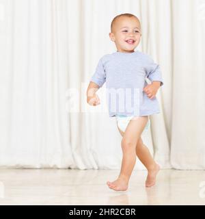 Sein Zeug stolziert. Die ganze Aufnahme eines niedlichen kleinen Jungen, der in einem Windel- und T-Shirt durch das Haus läuft. Stockfoto