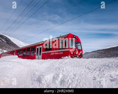 Cinuos-Chel, Schweiz - 3. Februar 2022: Roter Zug von Viafier retica, der zwischen Chur und Tirano in Italien fährt und die schneebedeckte Landschaft durchquert Stockfoto