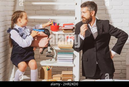 Schulmädchen studieren im Klassenzimmer mit Lehrer. Vater erklärt seiner Tochter zu Hause die Hausaufgaben. Hausaufgaben mit Papa machen. Stockfoto