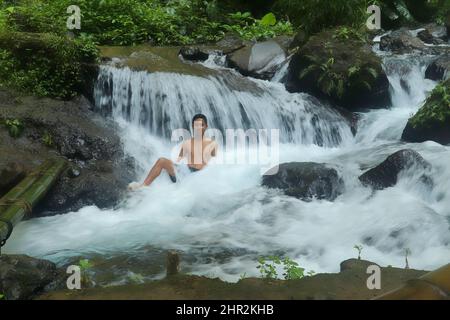 Ein junger Mann spritzt Wasser in den Fluss. Ein lächelnder junger Mann badet im Flusslauf Stockfoto