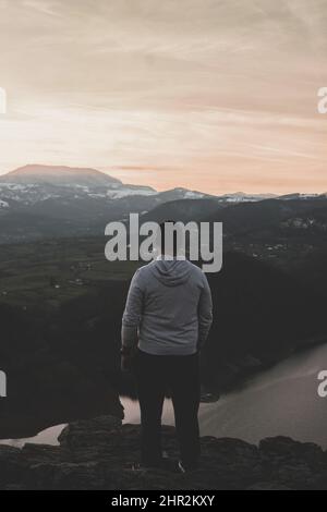 Einsamer Mann, der bei Sonnenuntergang die herrliche Berglandschaft beobachtet Stockfoto