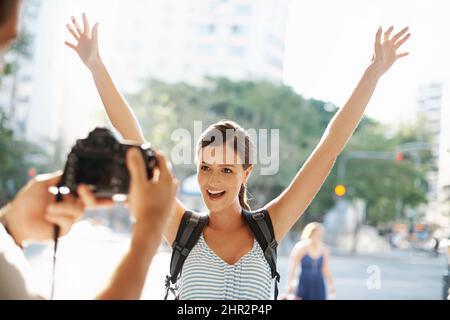 Begeistert von ihrem Urlaub. Ausgeschnittene Aufnahme einer jungen Frau, die für ein Bild posiert, während sie in einer fremden Stadt unterwegs ist. Stockfoto