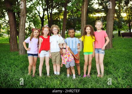Eine Gruppe von Vorschulkinder verschiedener Rassen umarmen und lächeln vor dem Hintergrund von Grün und einem Park. Kinderschutztag. Stockfoto
