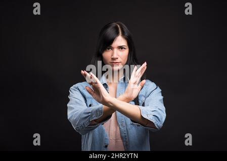 Attraktive kaukasische Brünette Mädchen im Hemd zeigt Stop-Geste isoliert auf schwarzem Studio-Hintergrund. Stockfoto