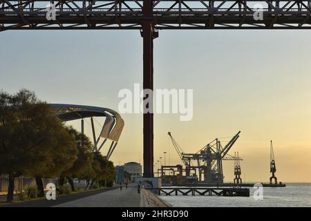 Morgenweg am Ufer des Flusses Tejo mit der Brücke Ponte 25 de Abril und dem Industriehafen im Hintergrund, Lissabon Portugal. Stockfoto