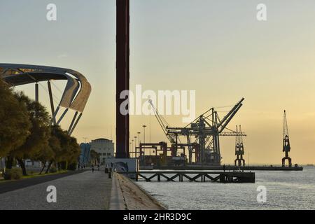 Morgenweg am Ufer des Flusses Tejo mit der Brücke Ponte 25 de Abril und dem Industriehafen im Hintergrund, Lissabon Portugal. Stockfoto