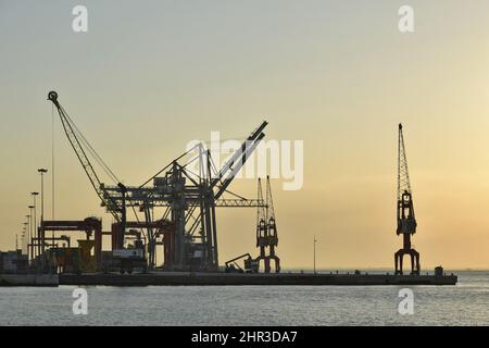 Industriehafen mit Kränen, die in Lissabon Portugal gegen den Morgenhimmel geschilhoutet wurden. Stockfoto